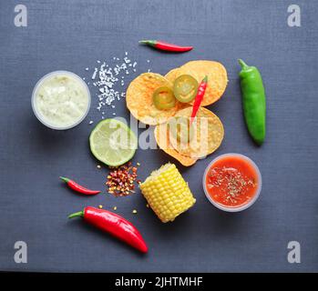 Ingredients for a nachos meal. Mexican food including nachos chips, peppers, chillies, salsa, sour cream dip, corn, jalapeno rings, lemon Stock Photo