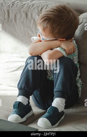 Child with autism in glasses sits on the sofa and sad Stock Photo