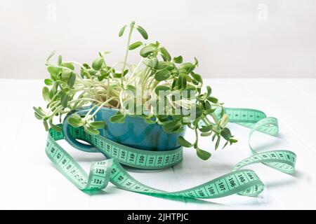 Measuring tape around blue mug with sunflower sprouts. White background. Top view Stock Photo