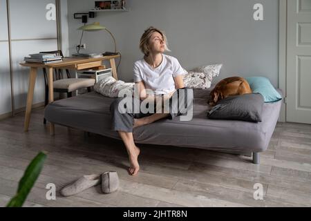 Sad thoughtful worried woman sit on sofa with dog looking away, feeling depressed and lonely Stock Photo