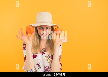European thin blonde attractive woman in her mid 20s wearing a hat and a floral blouse showing to the camera two juicy oranges over orange background. High quality photo Stock Photo
