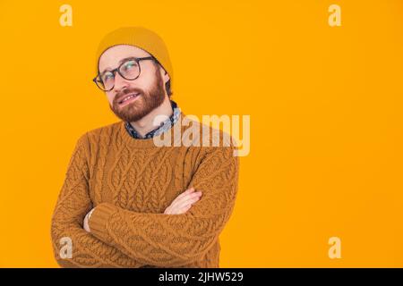 Thoughtful bearded Hipster in his 30s wearing the sweater and winter hat thinking - orange background. High quality photo Stock Photo