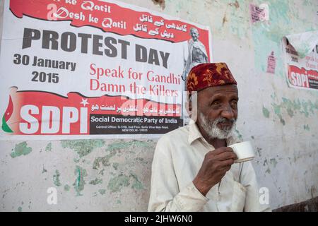 A man (blind in one eye) drinks a cup of tea in front of a SDPI political poster in Bijapur, India Stock Photo