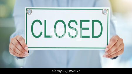 Sorry, were closed. an unrecognizable businesswoman holding up a closed sign while standing in the office. Stock Photo