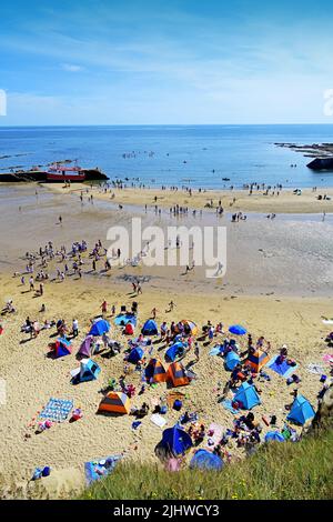 Cullercoats Bay beach vista lots of people enjoying the sunshine with canoeists surfers paddle boarders tents people picnicing fishing boat by the pie Stock Photo