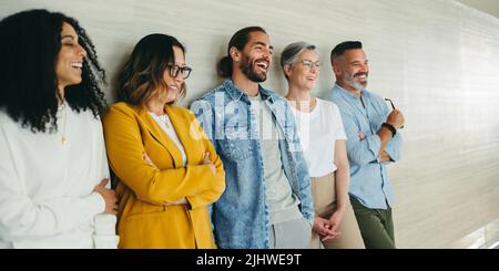 Successful business team laughing cheerfully while standing together against a wall. Group of multicultural businesspeople working together in a moder Stock Photo