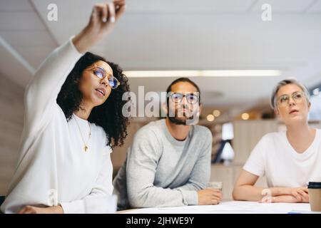 Smart businesswoman sharing her ideas with her team during a meeting. Group of creative design professionals having a discussion while working on a ne Stock Photo
