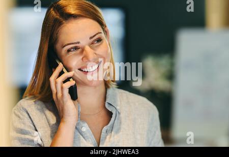Happy female entrepreneur smiling cheerfully while speaking on a phone call. Successful businesswoman communicating with her business associates in a Stock Photo