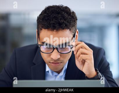 Let me read this over once more. a young businessman working on a laptop in an office. Stock Photo
