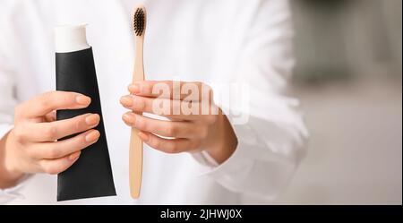 Woman with tube of activated charcoal tooth paste and bamboo brush, closeup Stock Photo