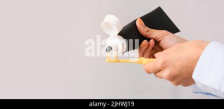 Woman applying activated charcoal tooth paste onto brush against grey background, closeup Stock Photo
