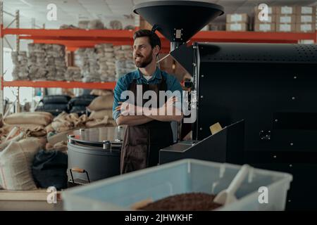 Portrait of smiling business owner on background of own small coffee factory looking away Stock Photo