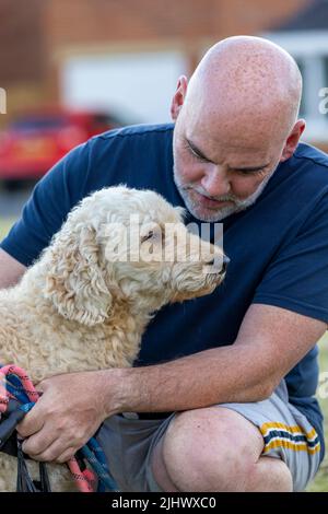 Affectionate moment between a middle aged man and his beautiful beige coloured Labradoodle dog Stock Photo