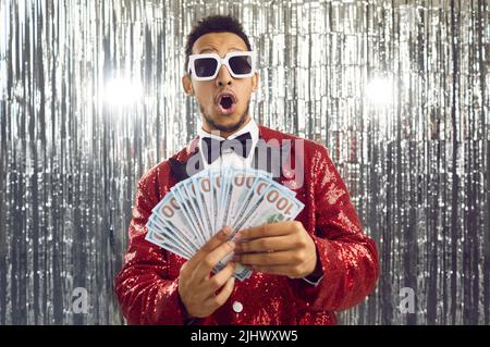 Happy surprised young guy who has won cash prize is holding bunch of money bills Stock Photo