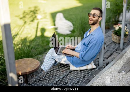 Man works on laptop while sitting at backyard Stock Photo