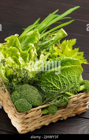 Set of green fresh vegetables and herbs in wicker basket. Top view. Dark wooden background Stock Photo