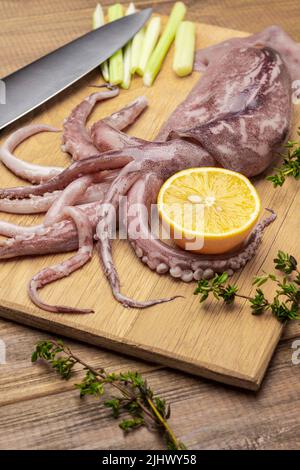 Raw squid with tentacles, lemon and knife on cutting board. Top view. Wooden background Stock Photo