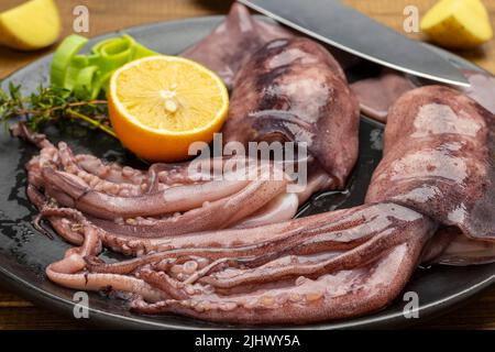 Fresh squid with tentacles, lemon and knife on black plate. Close up. Top view Stock Photo