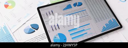 Workplace mess filled with with business papers, tablet with diagrams and charts on device screen Stock Photo