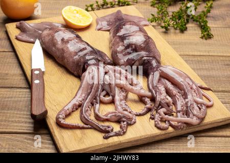 Two raw tentacled squids, knife and lemon on cutting board. Top view. Wooden background Stock Photo