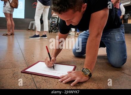 A young Hispanic man sitting on the floor and writing an airport welcome greeting Stock Photo