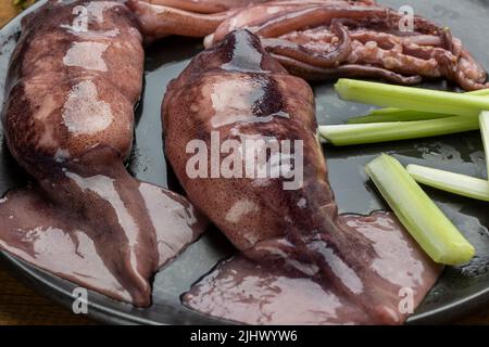 Raw squid with tentacles and celery stalks on black plate. Close up. Top view Stock Photo