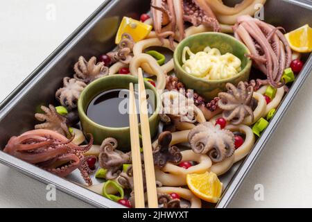 Bamboo sticks on bowl with soy sauce among seafood in baking tray. Top view. White background Stock Photo