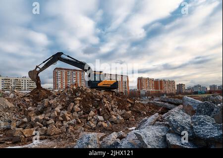 Excavator pours soil on pile of garbage at demolition site Stock Photo