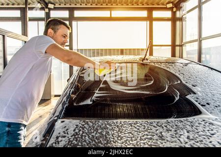 A man washes his car with foam at a self-service car wash. Stock Photo