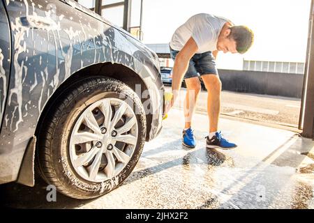 A man washes his car with foam at a self-service car wash. Stock Photo