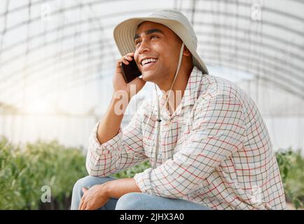 Buyers are always keen for his fresh crops. a young man talking on a cellphone while working on a farm. Stock Photo