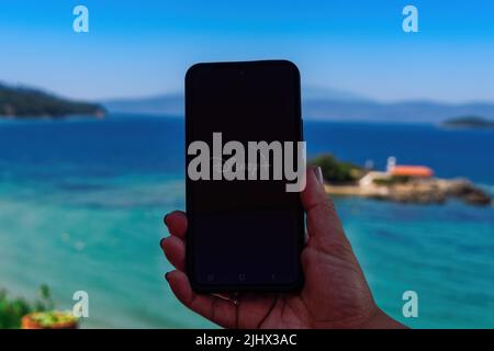 Female with mobile phone in hand, views screen with Disney+ streaming provider intro page against outdoors beach background. Stock Photo