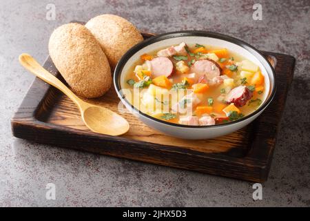 Portion of hot pea soup with potatoes, onions, carrots, bacon and sausages close-up in a bowl on the table. Horizontal Stock Photo