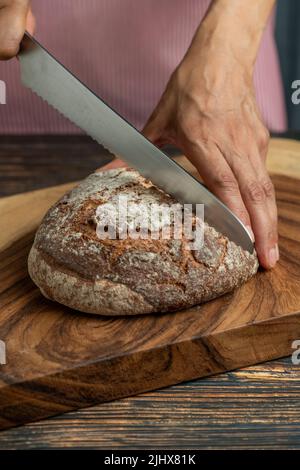 Hands of a woman holding and cutting a rustic sourdough bread with knife - stock photo Stock Photo