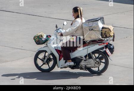 SAMUT PRAKAN, THAILAND, MAY 26 2022, A woman rides a motorcycle with a storage box down the street Stock Photo
