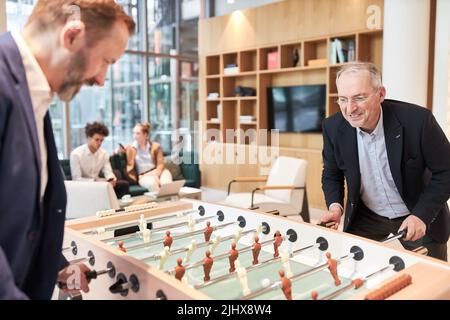 Business people play foosball at the foosball table during a break in the office lounge Stock Photo