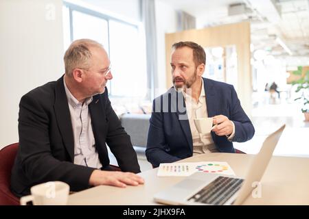 Two business people as colleagues having a casual conversation at the desk in the office Stock Photo