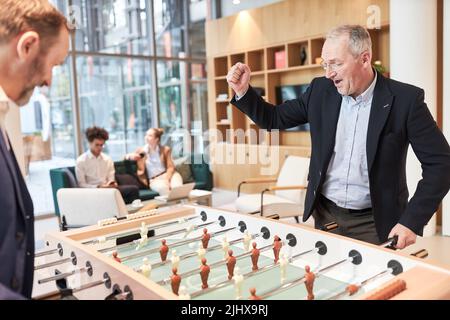 Businessman cheering with clenched fist while playing soccer at foosball table in office Stock Photo