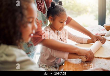 Females only, happy mixed race family of three cooking in a messy kitchen together. Loving black single parent bonding with her daughters while Stock Photo