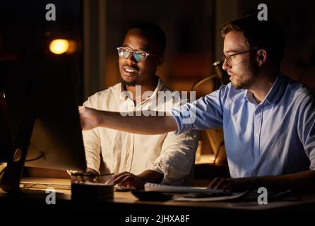 Lets try it this way and see if it works better. two businessmen working together on a computer in an office at night. Stock Photo