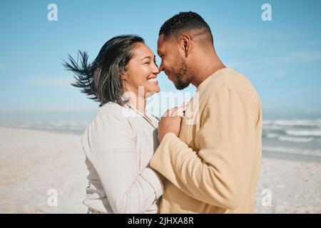 Loving young mixed race couple touching noses while dancing on the beach. Happy young man and woman in love enjoying romantic moment while on Stock Photo
