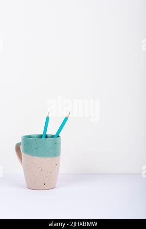 Cup With Two Pencils Inside Placed On Desk. Mug With Pens On Table. Case With Writing Items In It. Casing With Office Supplies. Stock Photo
