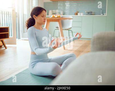 Beautiful young mixed race woman meditating in the asana position while practicing yoga at home. Hispanic female exercising her body and mind, finding Stock Photo
