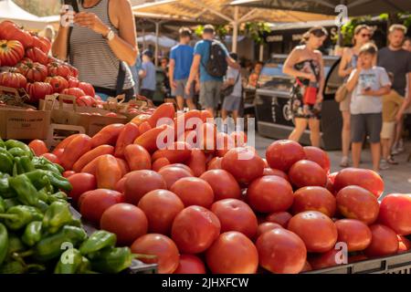 Open-air stall selling Mediterranean vegetables. Green peppers and tomatoes. Island of Mallorca, Spain. In the background, out of focus, customers in Stock Photo