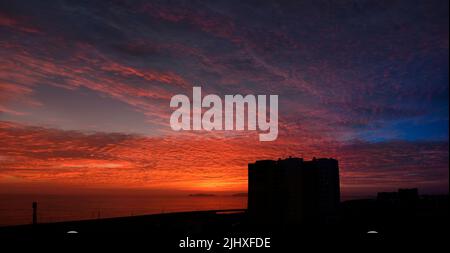 Twilight sky after sunset, clouds in red, orange ,blue, violet, purple, crimson colors. Silhouettes of building. Colorful scenery skyline background. Stock Photo