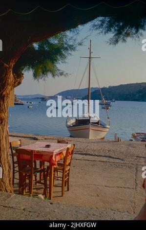 Boats moored in bay with café table on quaside, Sifnos, Greece Stock Photo