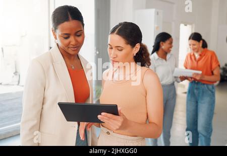 Two mixed race businesswomen talking and working on a digital tablet together at work. Hispanic businesspeople talking and planning while looking at a Stock Photo