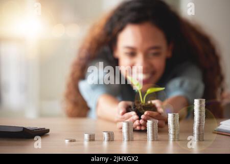 African American woman holding a growing plant in her hands while counting her savings. Stacks of coins symbolising positive financial growth, goals Stock Photo