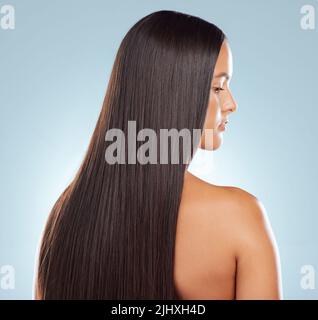 Rear view of a brunette woman with long lush beautiful hair posing against a grey studio background. Mixed race female standing showing her beautiful Stock Photo