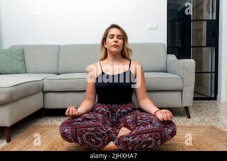 pretty young blonde woman meditating in the living room at home Stock Photo